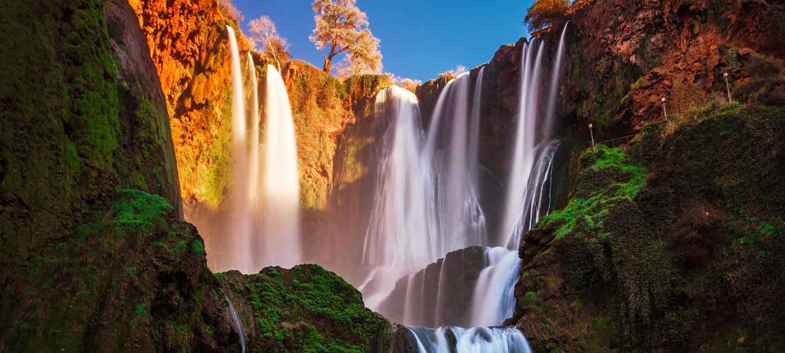 The Ouzoud Waterfalls in late afternoon light, falling from red cliffs into the gorge